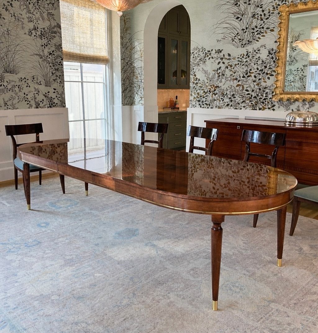 Polished dark wood oval dining table with gold accents in an elegant room