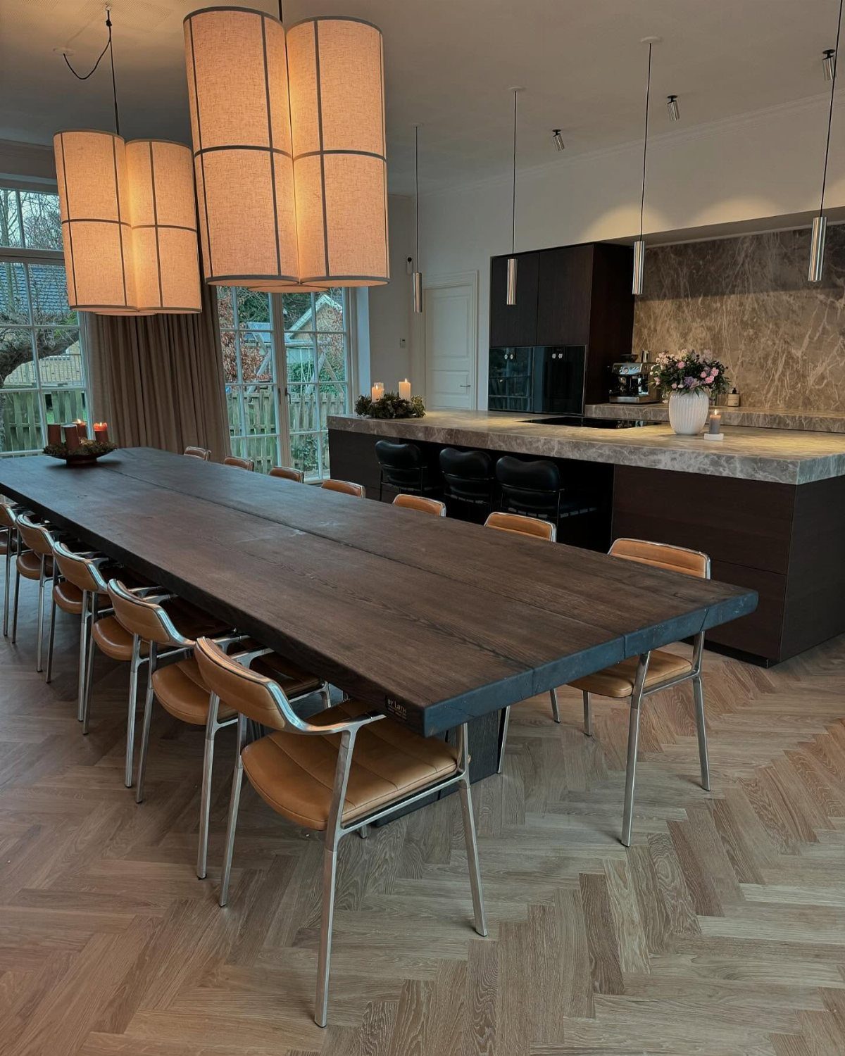 Long dark wood dining table with tan leather chairs on herringbone wood floors