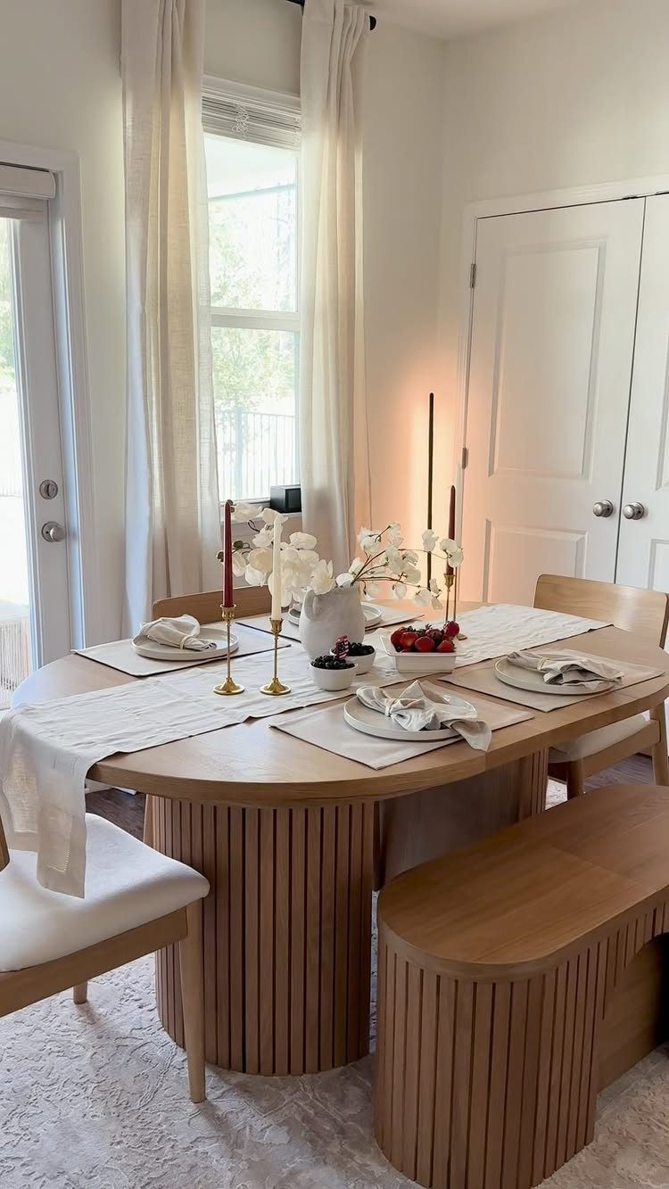 Oval light-wood dining table with ribbed base and matching bench in bright room