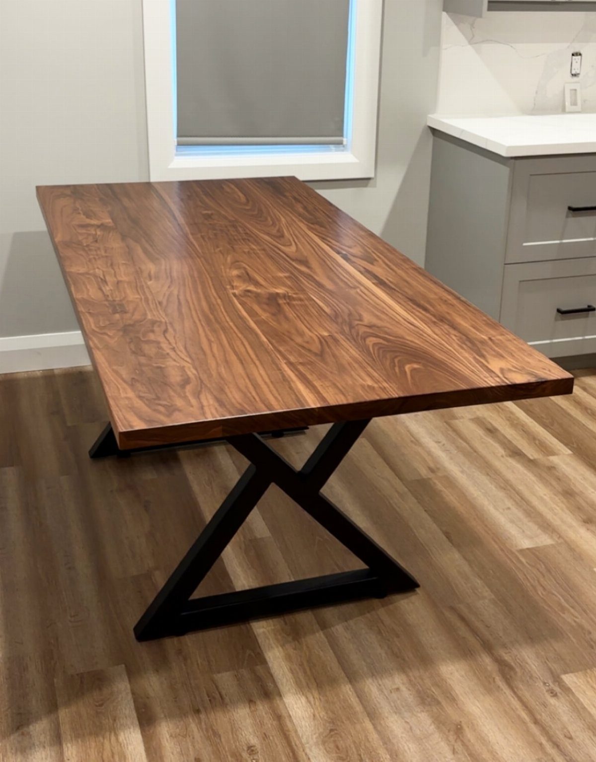 Long walnut dining table with black metal X-legs on light wood flooring