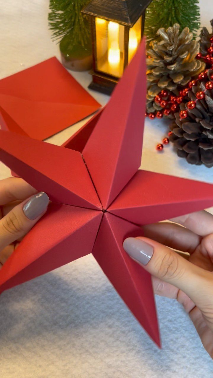 Red 3D paper star held by hands with festive holiday decorations in background