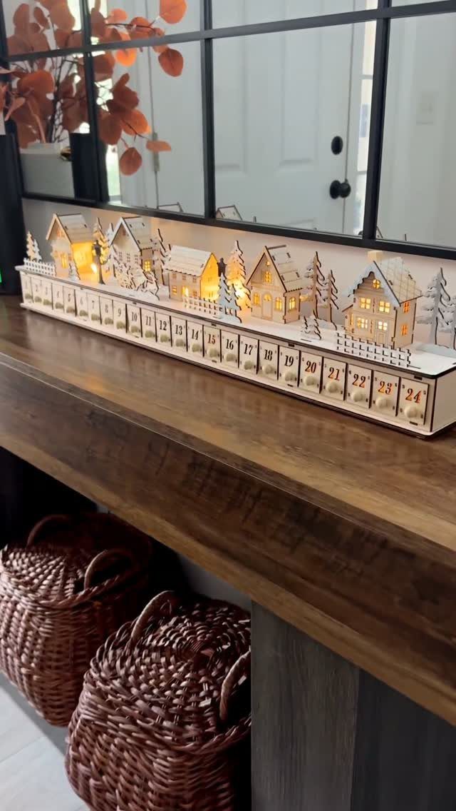 Wooden advent calendar with illuminated miniature village houses on a brown wooden table.