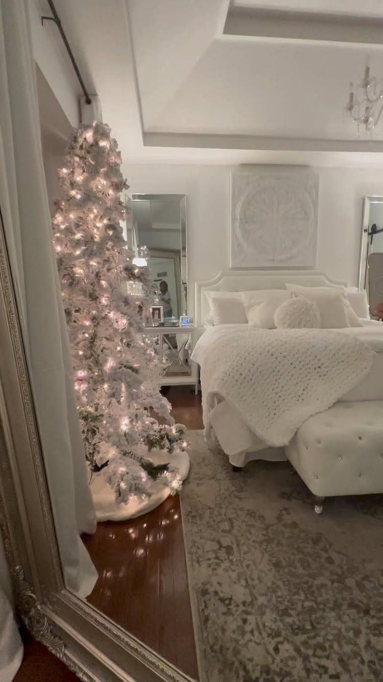 White flocked Christmas tree with lights in a bright, all-white bedroom setting