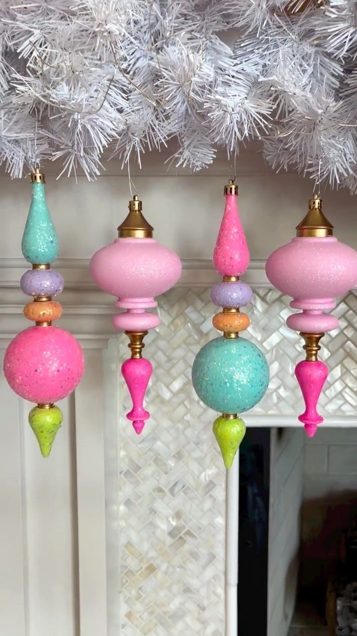 Colorful glittery Christmas ornaments hanging from a white artificial pine garland over a mantel.