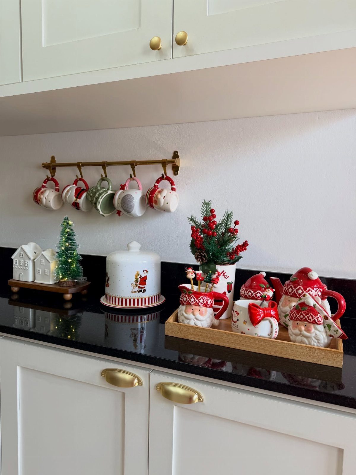 Christmas-themed kitchen counter with Santa mugs, a small lit tree, and hanging mugs.