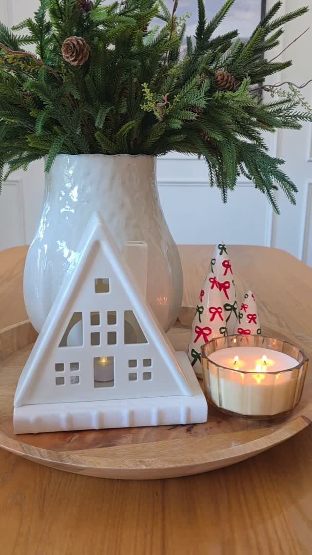 White ceramic house candle holder and evergreen branches on a wooden tray