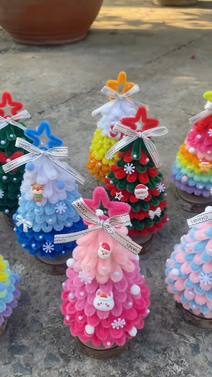 Colorful pom-pom Christmas tree ornaments with ribbons and stars on a stone surface.