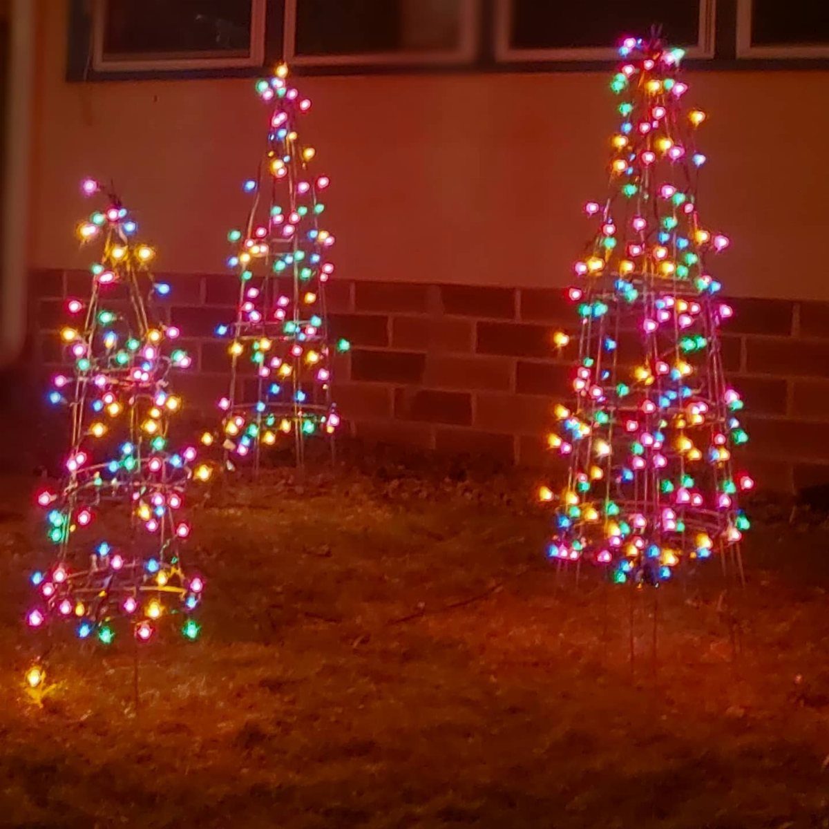 Three wire cone frames wrapped in colorful Christmas lights on a grassy lawn