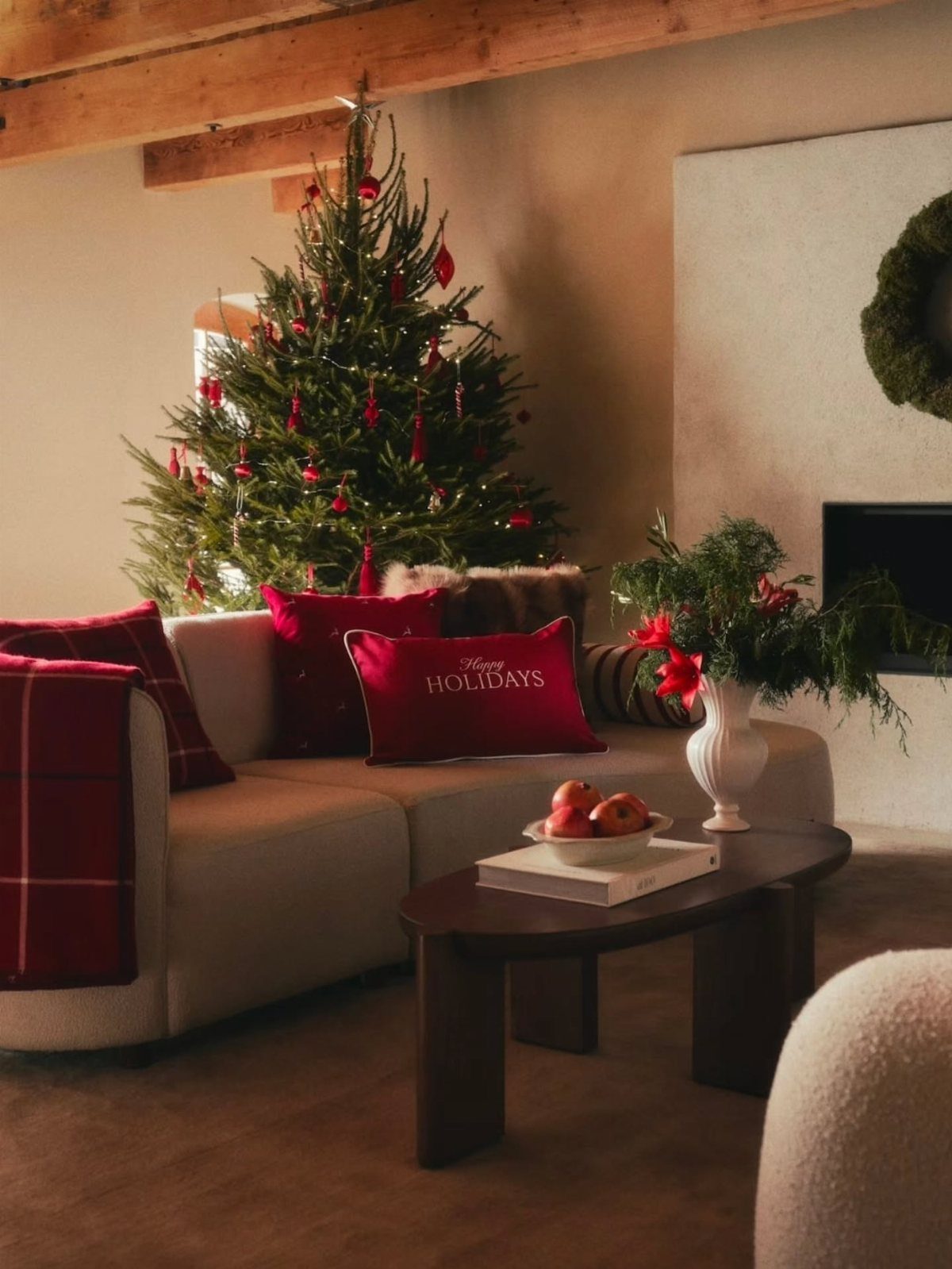 Beige sofa with red holiday pillows and a plaid throw near a Christmas tree.