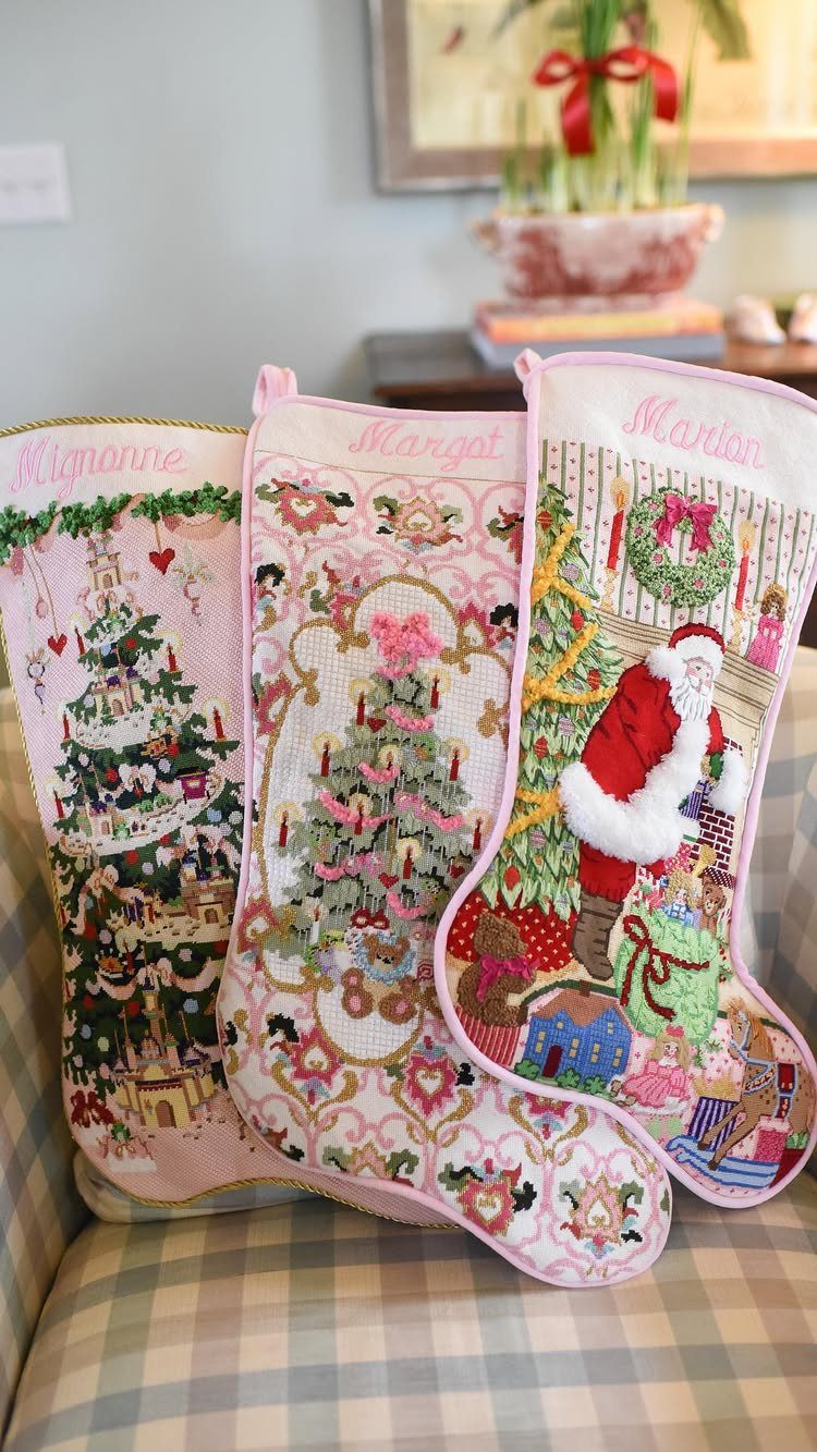 Three pink embroidered Christmas stockings with personalized names and festive holiday scenes.
