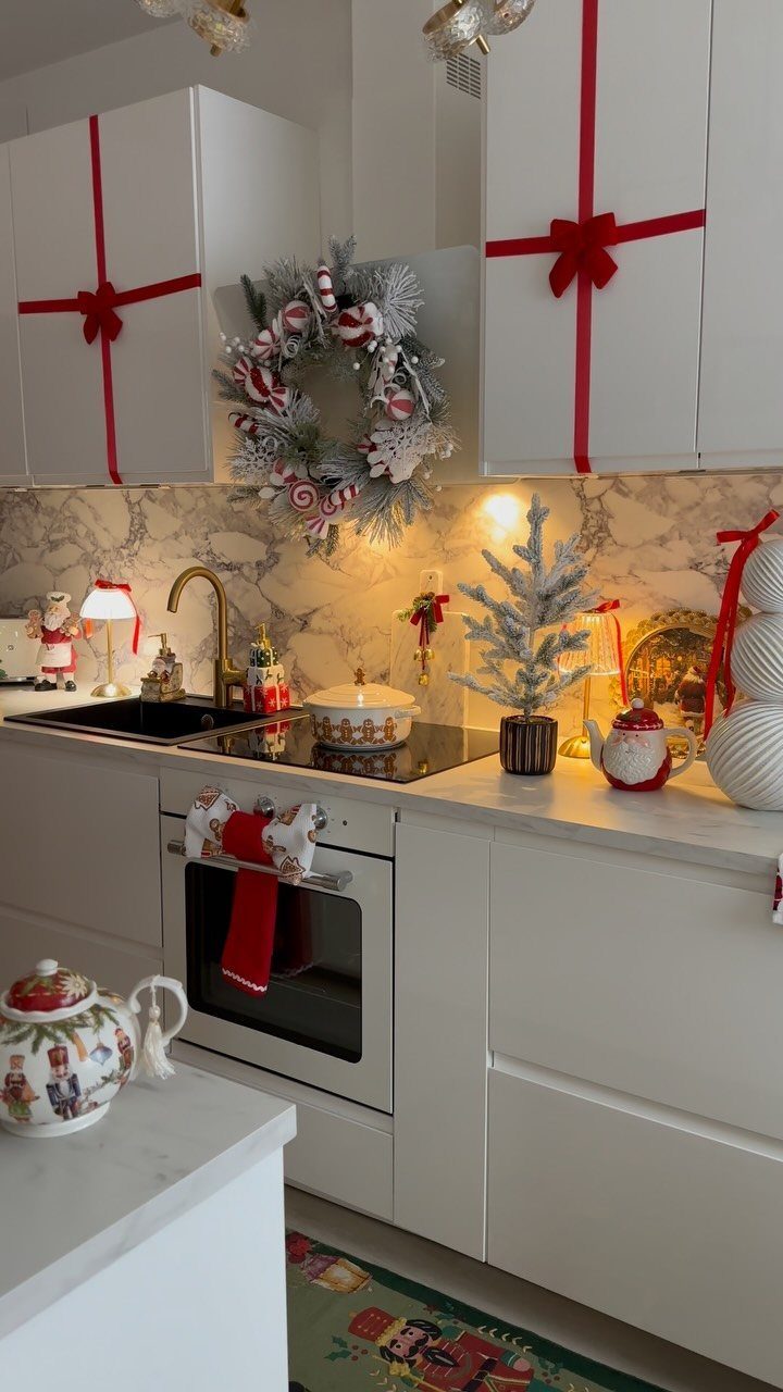White kitchen cabinets decorated with red ribbons and a frosted Christmas wreath.