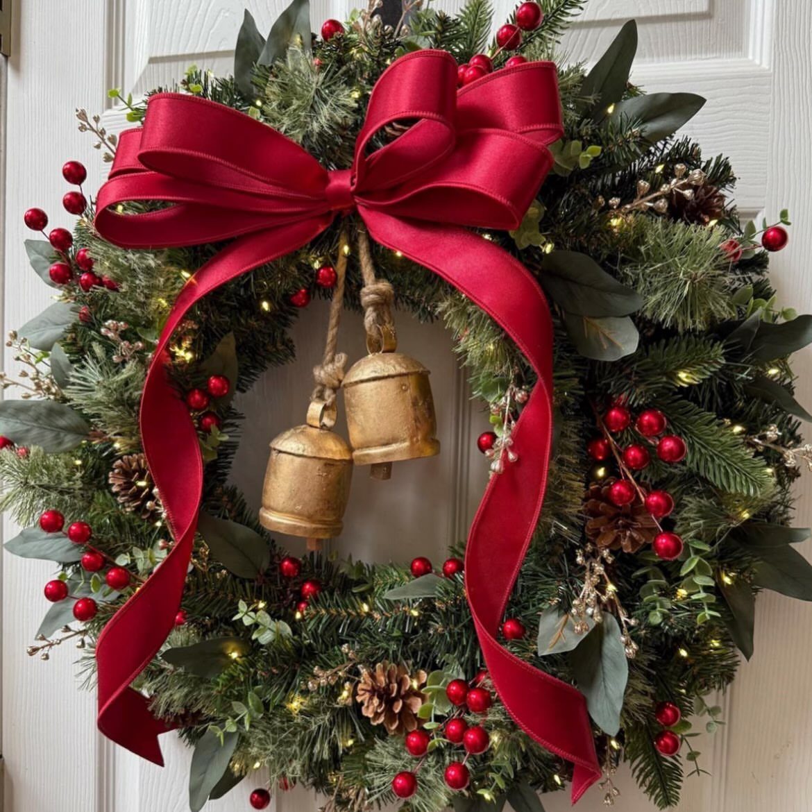 Christmas wreath with red berries, gold bells, and a large red bow on white door