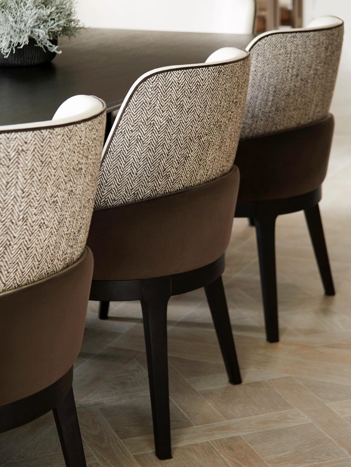Upholstered dining chairs with herringbone fabric and brown seats around a dark table.