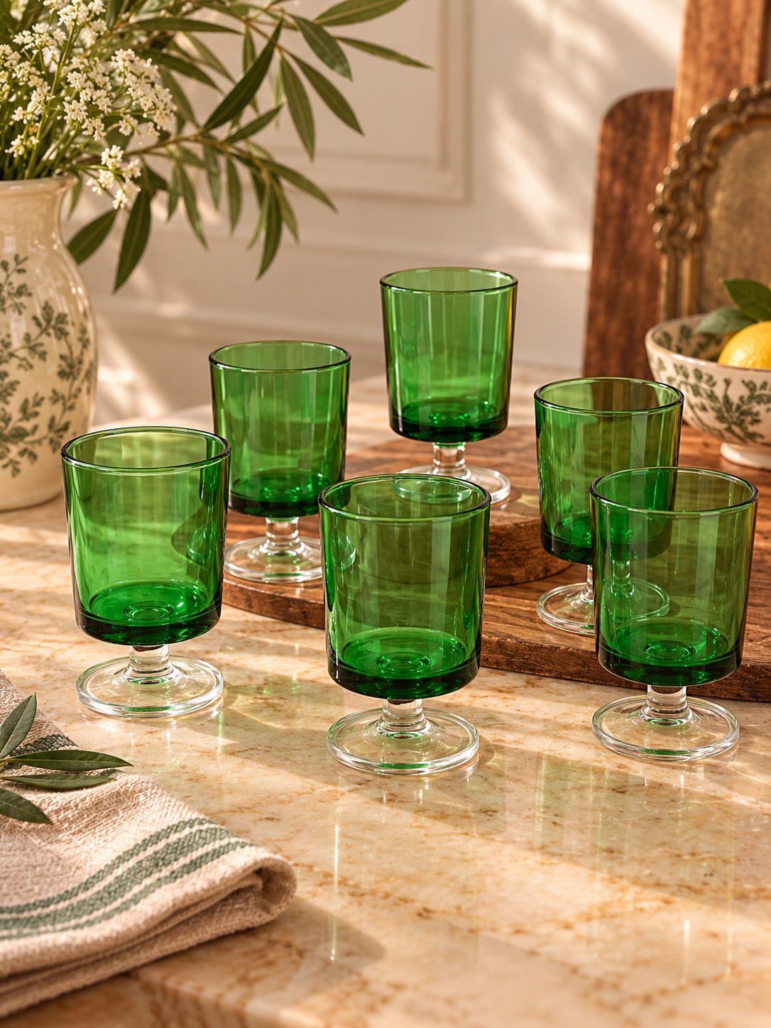Green tinted glass goblets arranged on a wooden board and marble surface.