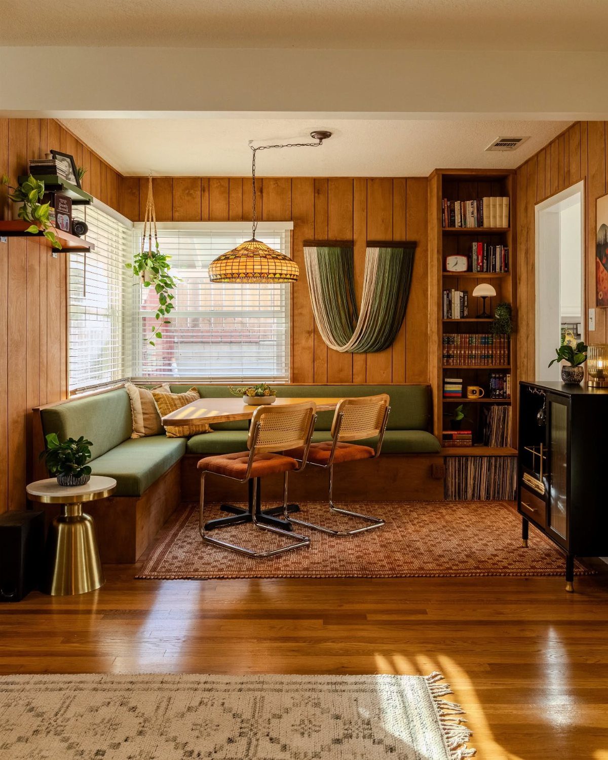 Dining nook with brown wood paneling, green banquette seating, and woven chairs.