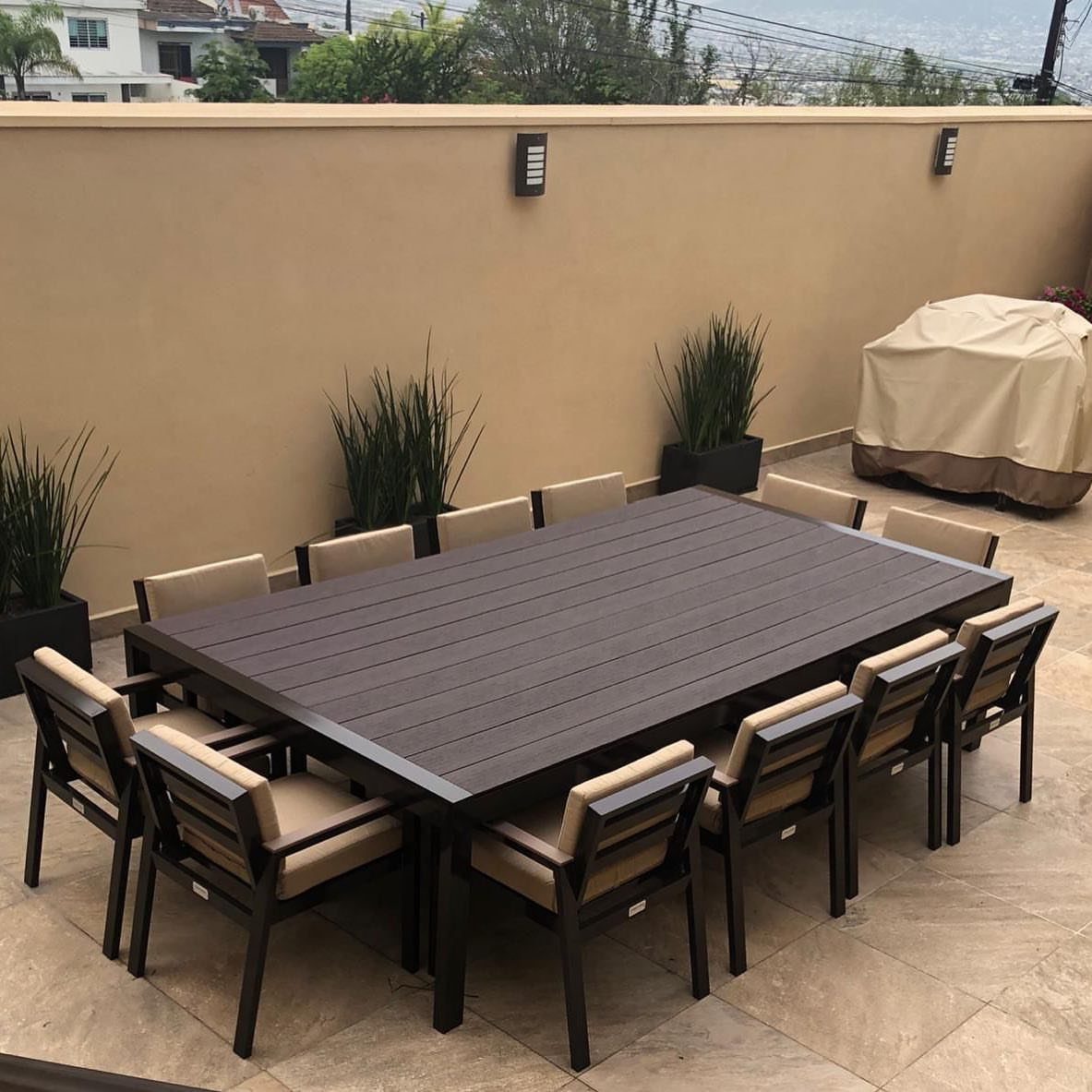 Large dark brown rectangular outdoor dining table with beige cushioned chairs on a patio.