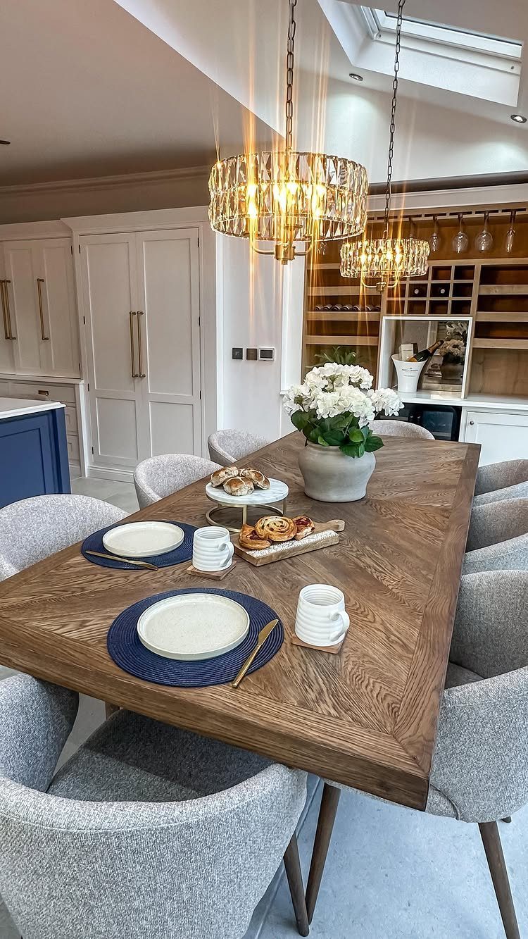 Wooden rectangular dining table with grey chairs and crystal chandeliers in a bright room