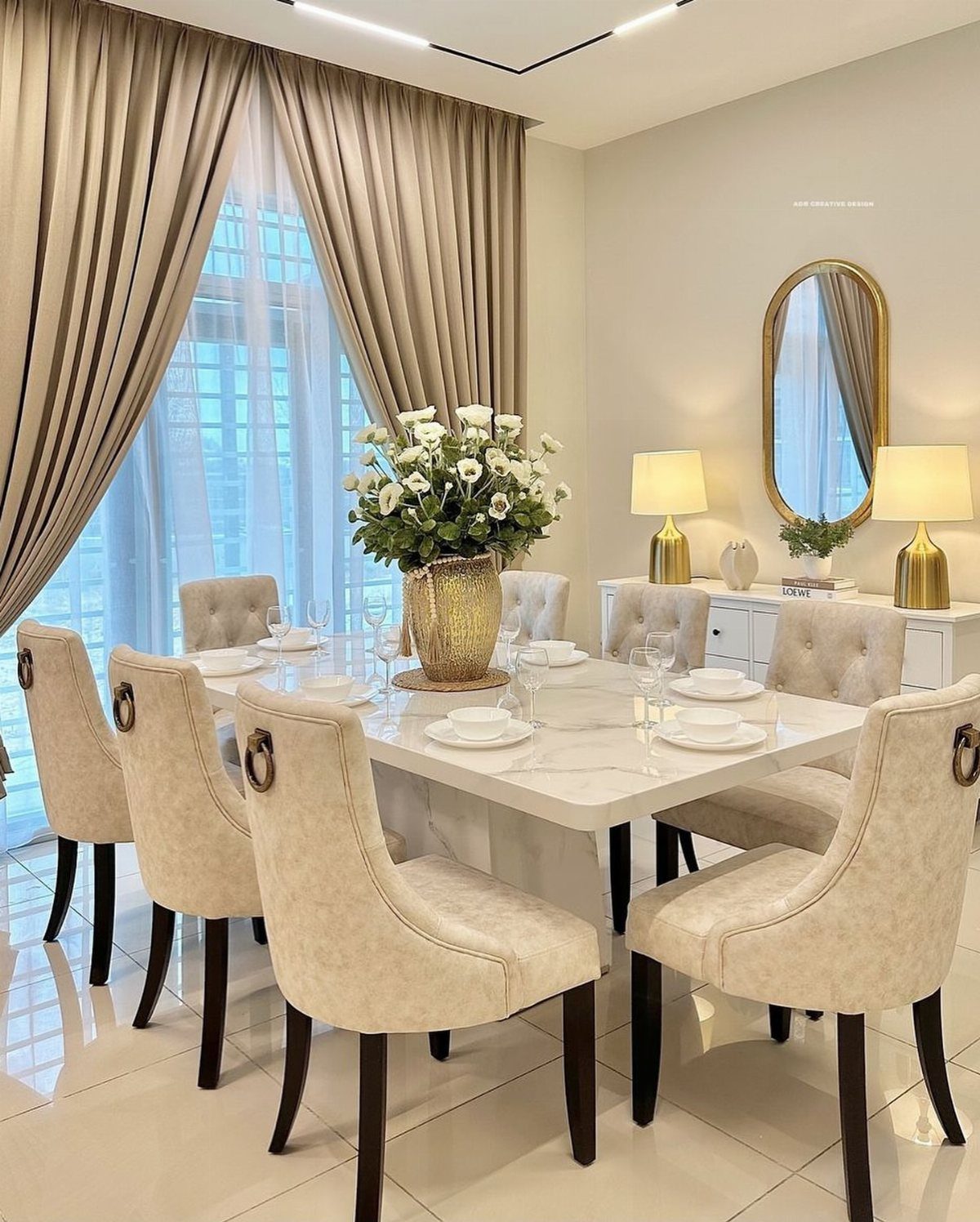 White marble dining table with beige upholstered chairs and white floral centerpiece.