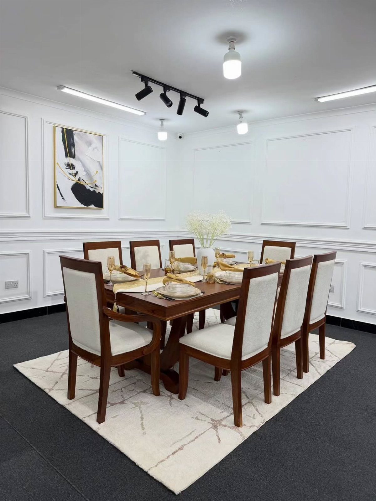 Rectangular wooden dining table with eight matching white upholstered chairs on a marble rug.