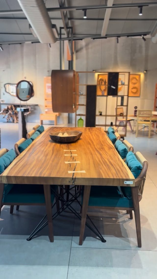 Rectangular wooden dining table with resin-filled crack and teal cushioned chairs in showroom