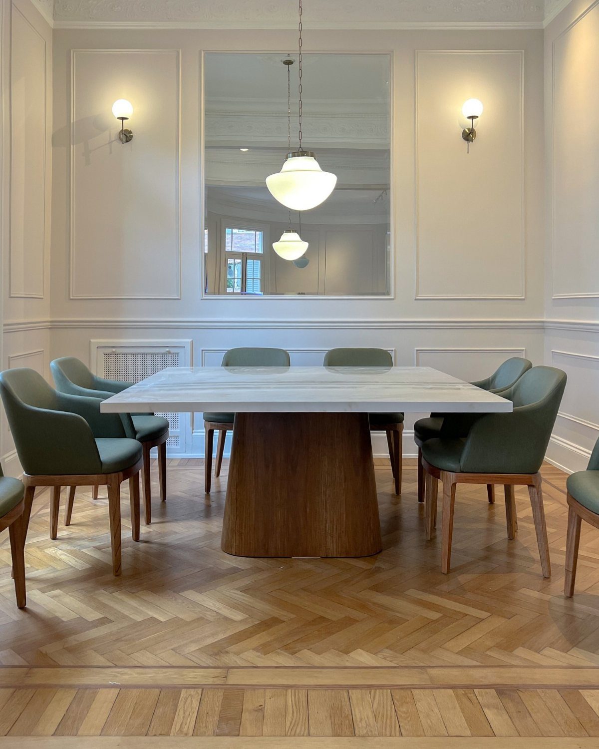 White marble dining table with eight green chairs in a bright, modern room.