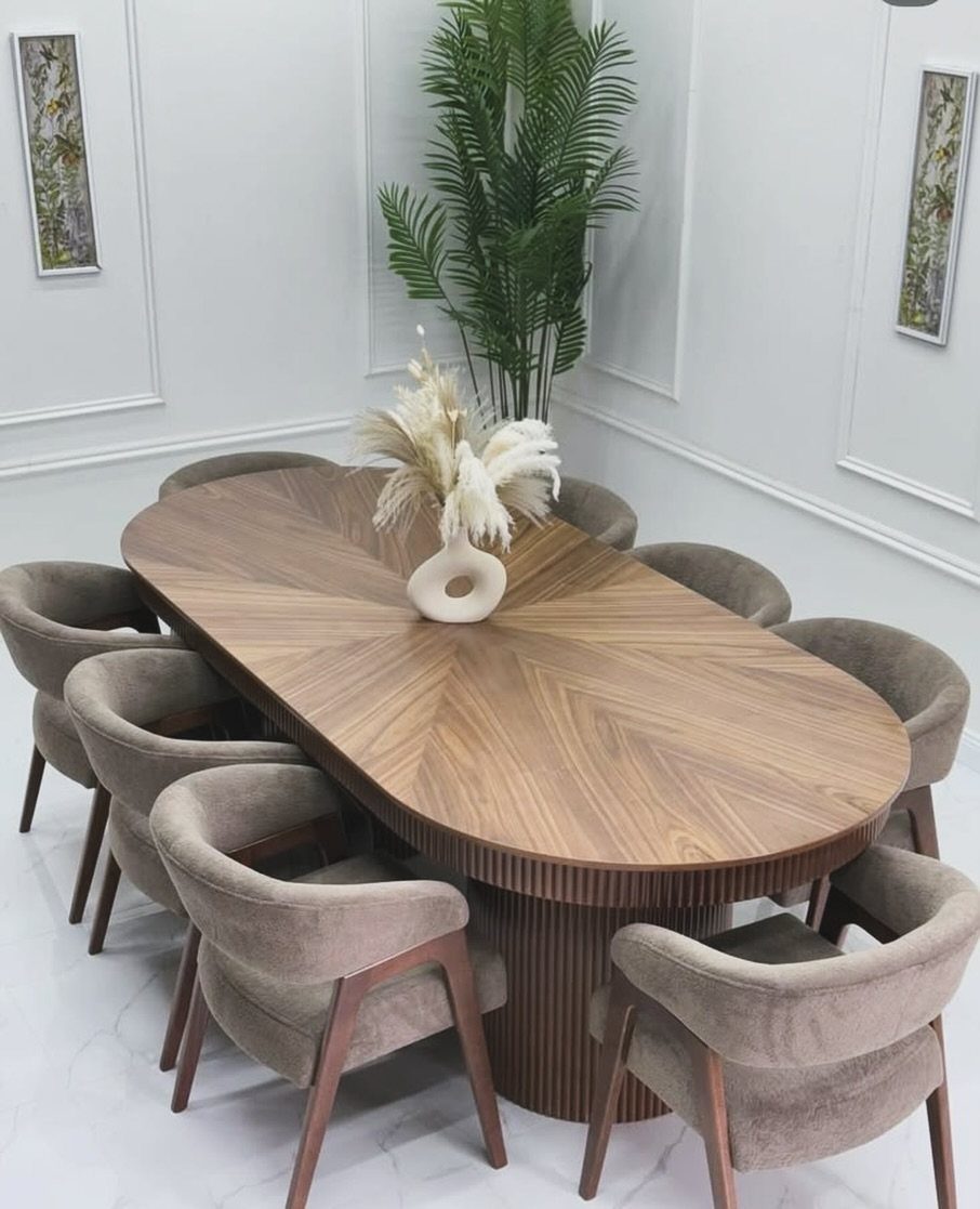 Oval wooden dining table with eight grey upholstered chairs in a white room