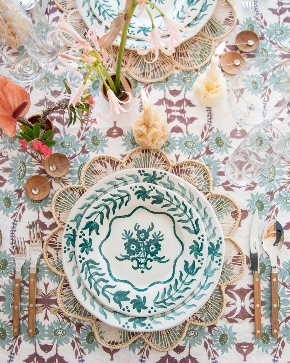 Patterned green and white ceramic plates on woven rattan placemats over floral tablecloth.