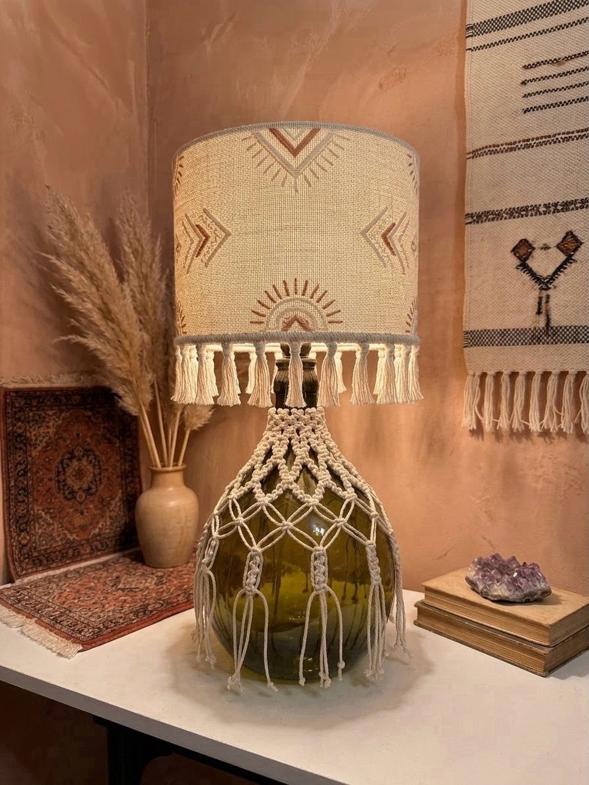 Boho table lamp with macrame base and fringed shade on a white table.