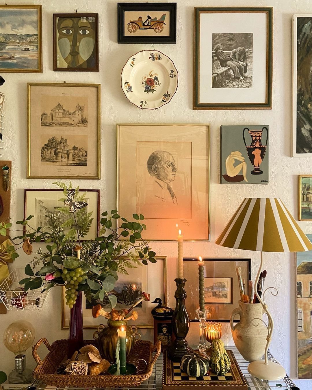 Gallery wall with eclectic framed art and a floral plate above a decorated table.