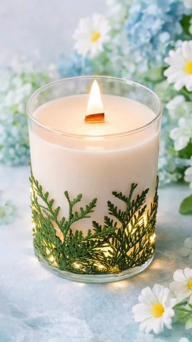 Lit white candle in a glass jar decorated with evergreen sprigs and fairy lights.