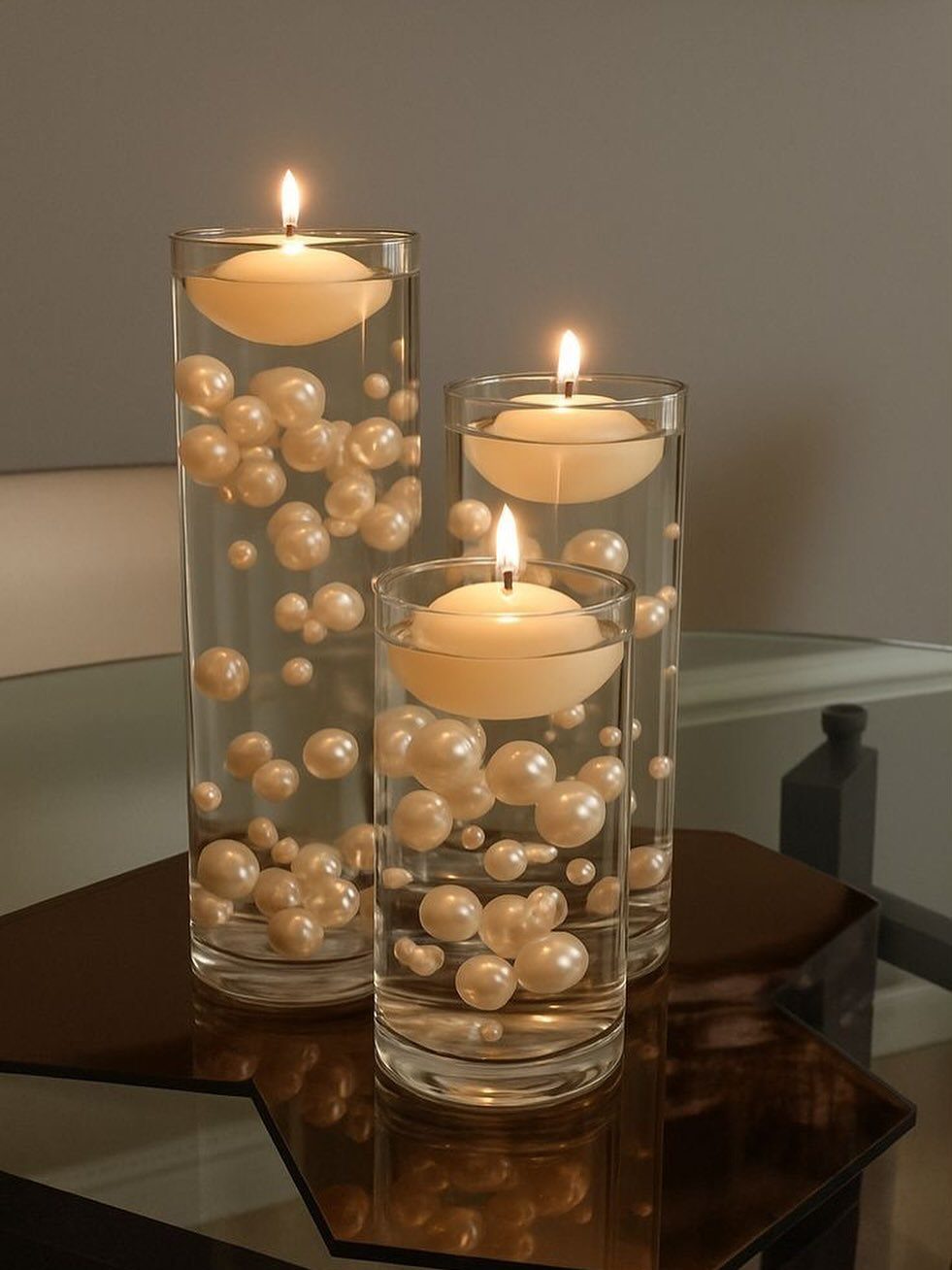 Floating white candles and pearls in three tall glass cylinder vases on a table