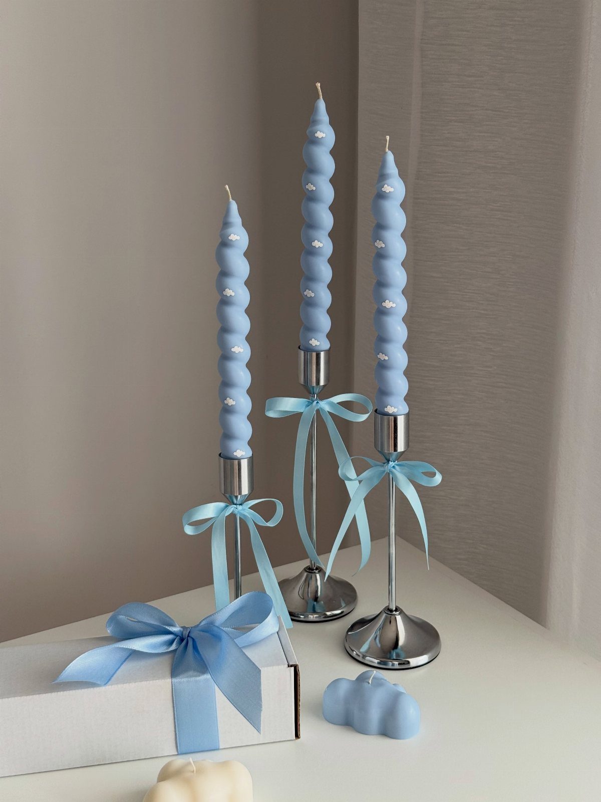 Three blue spiral taper candles in silver holders with blue ribbons on white surface