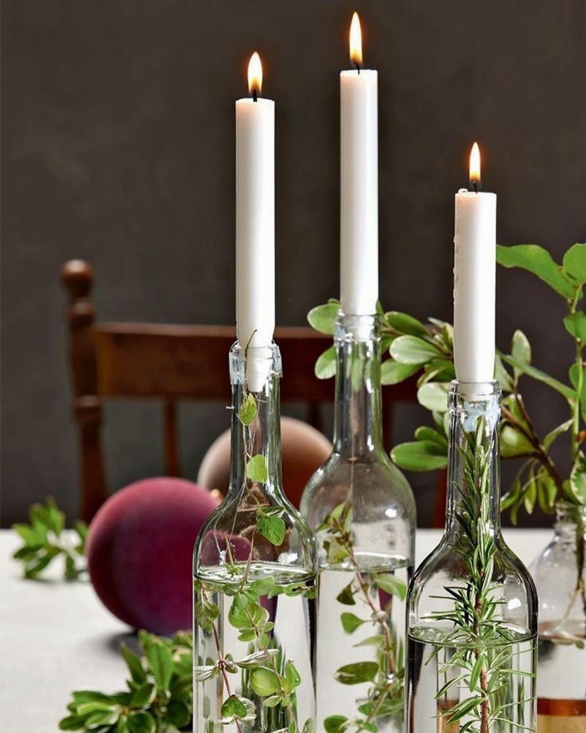 White taper candles in glass bottles with water and green foliage on a table