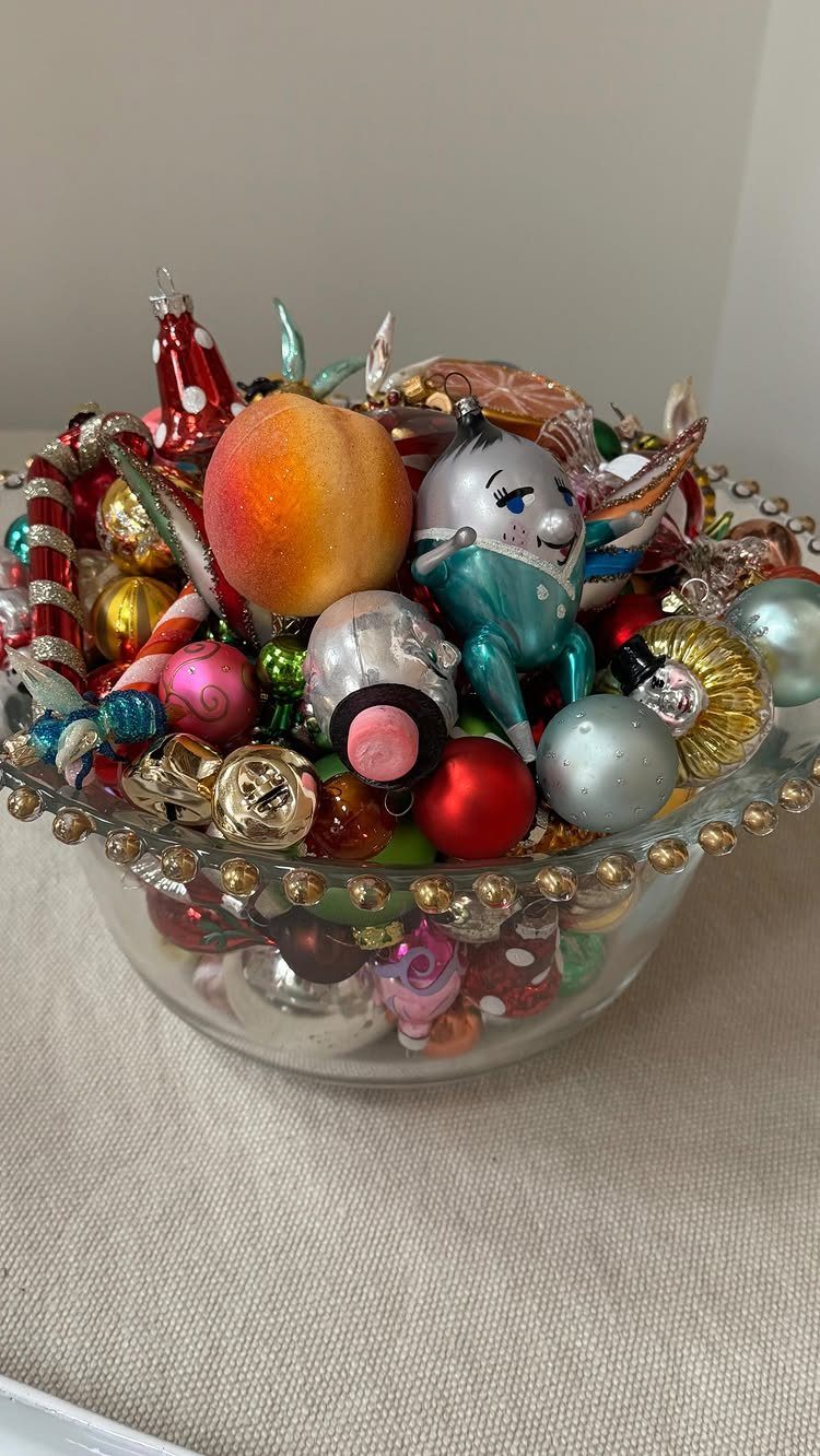 Glass bowl filled with colorful Christmas ornaments on a light fabric surface.