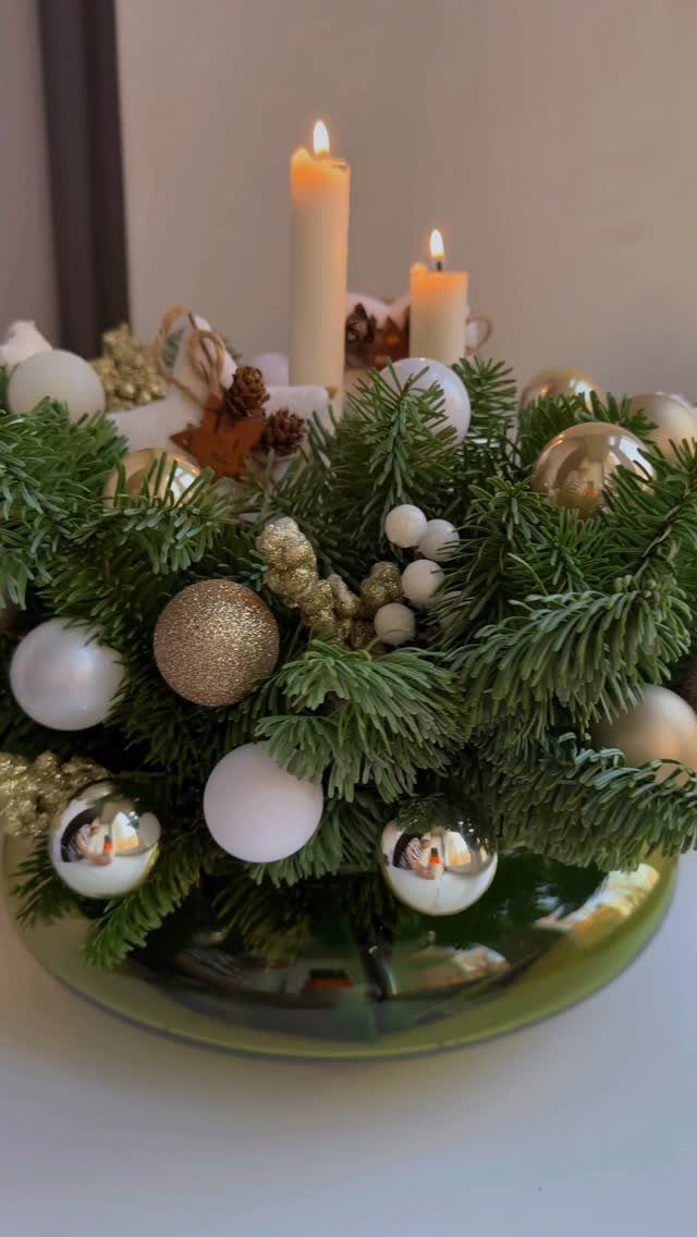 Evergreen arrangement with gold and white ornaments and lit candles on a tray