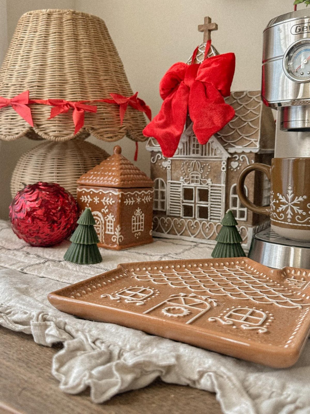 Festive tabletop display with ceramic gingerbread houses, red ornaments, and small green trees.