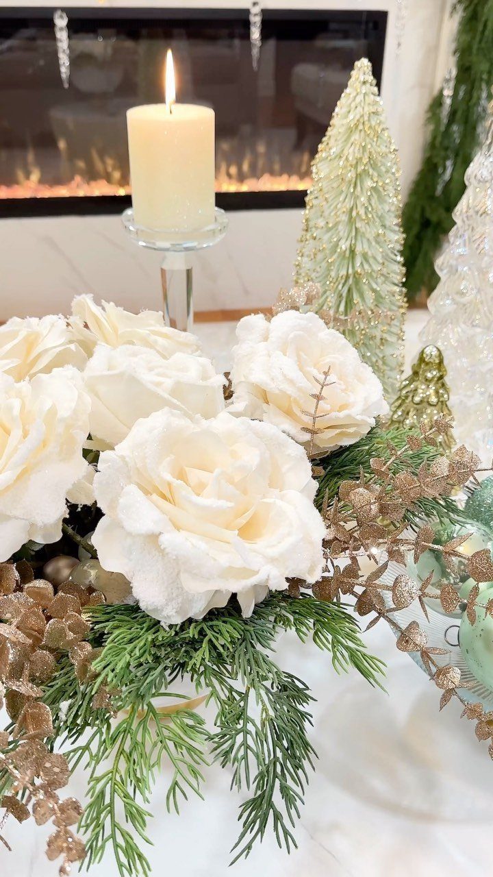White roses and gold Christmas decorations on a white coffee table near a fireplace