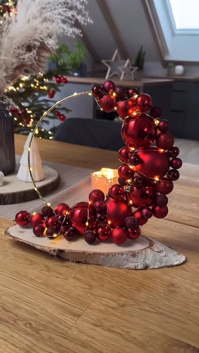 Crescent arrangement of red Christmas ornaments and lights on a wooden slice.
