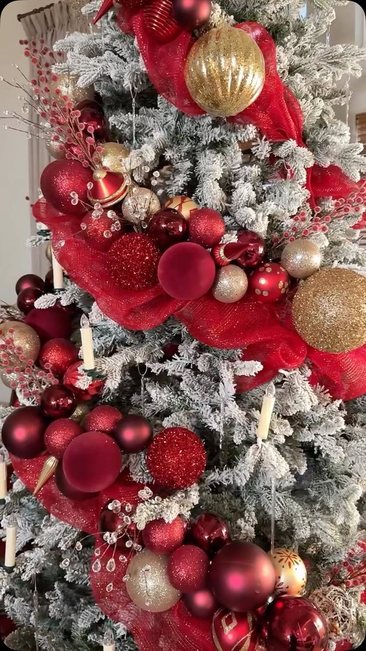 Flocked white Christmas tree decorated with red and gold ornaments and red ribbons.