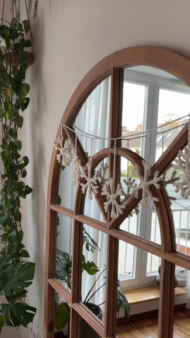 White snowflake ornaments hanging across a wooden arched mirror in a bright room