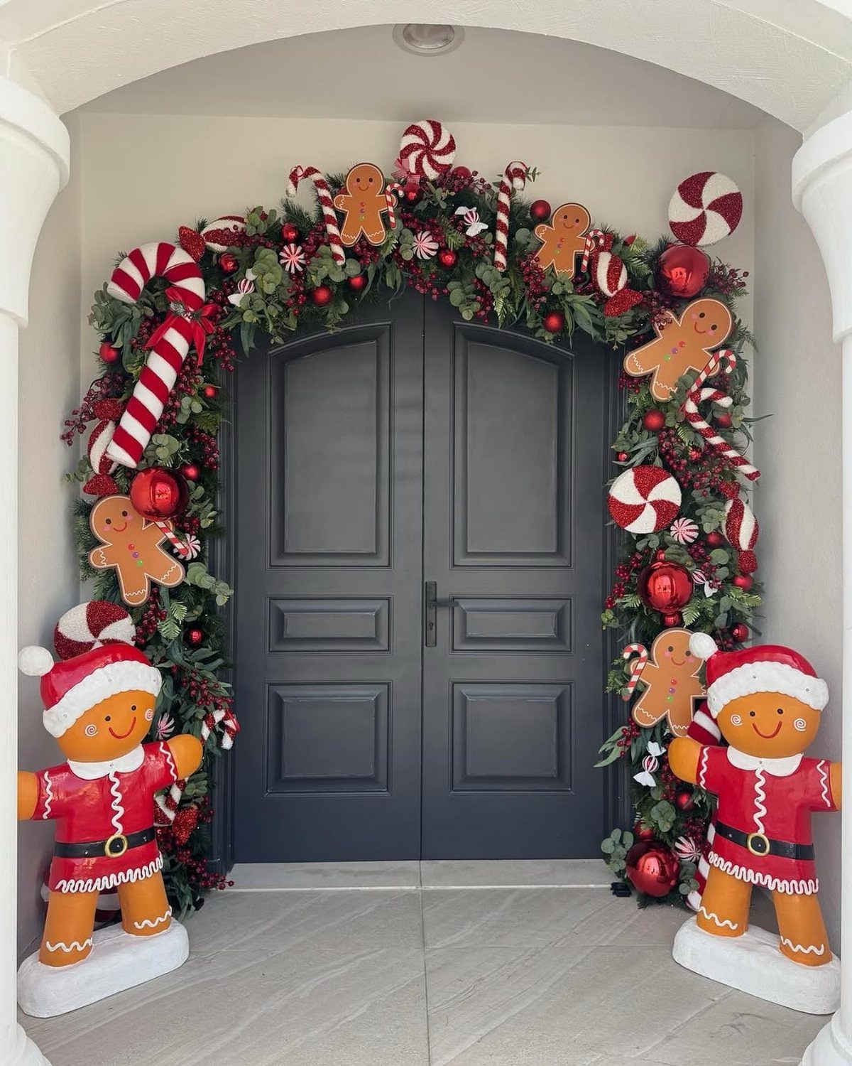 Evergreen garland with gingerbread men and peppermint candies framing a grey front door