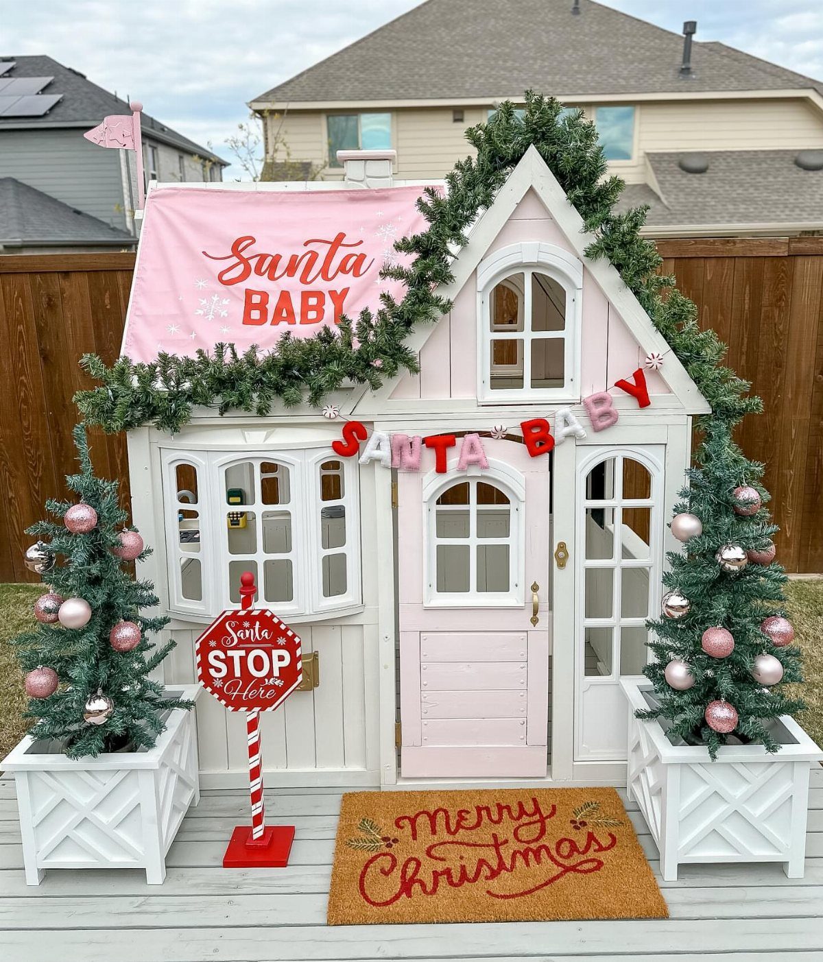 Decorated children's playhouse with Christmas garlands, small trees, and festive holiday signage.