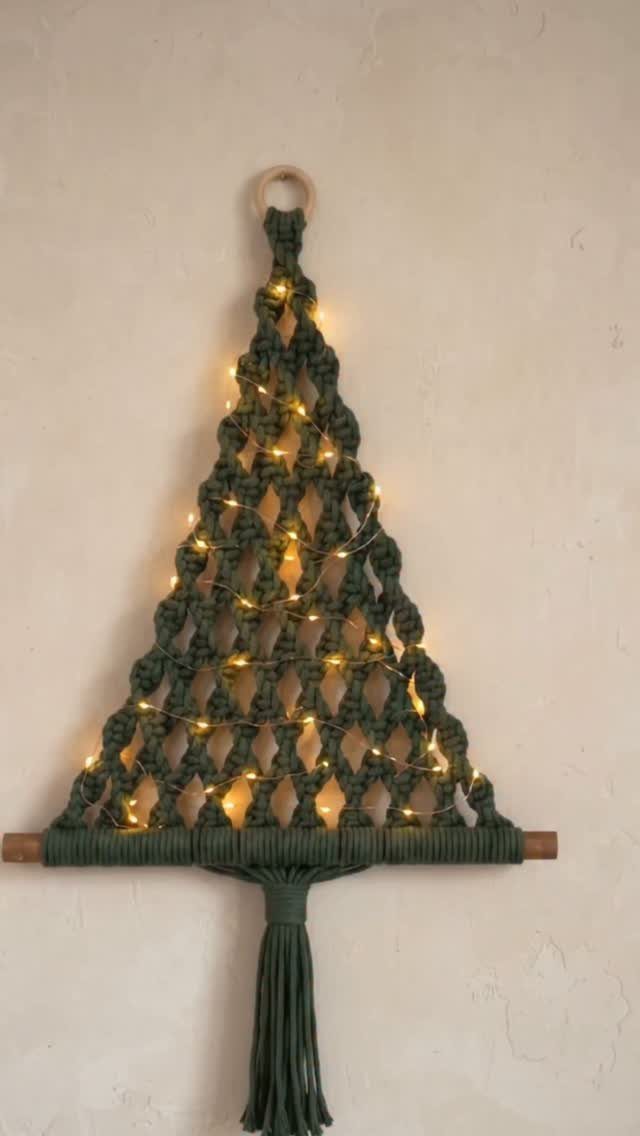 Green macrame Christmas tree wall hanging illuminated by warm yellow twinkle lights.