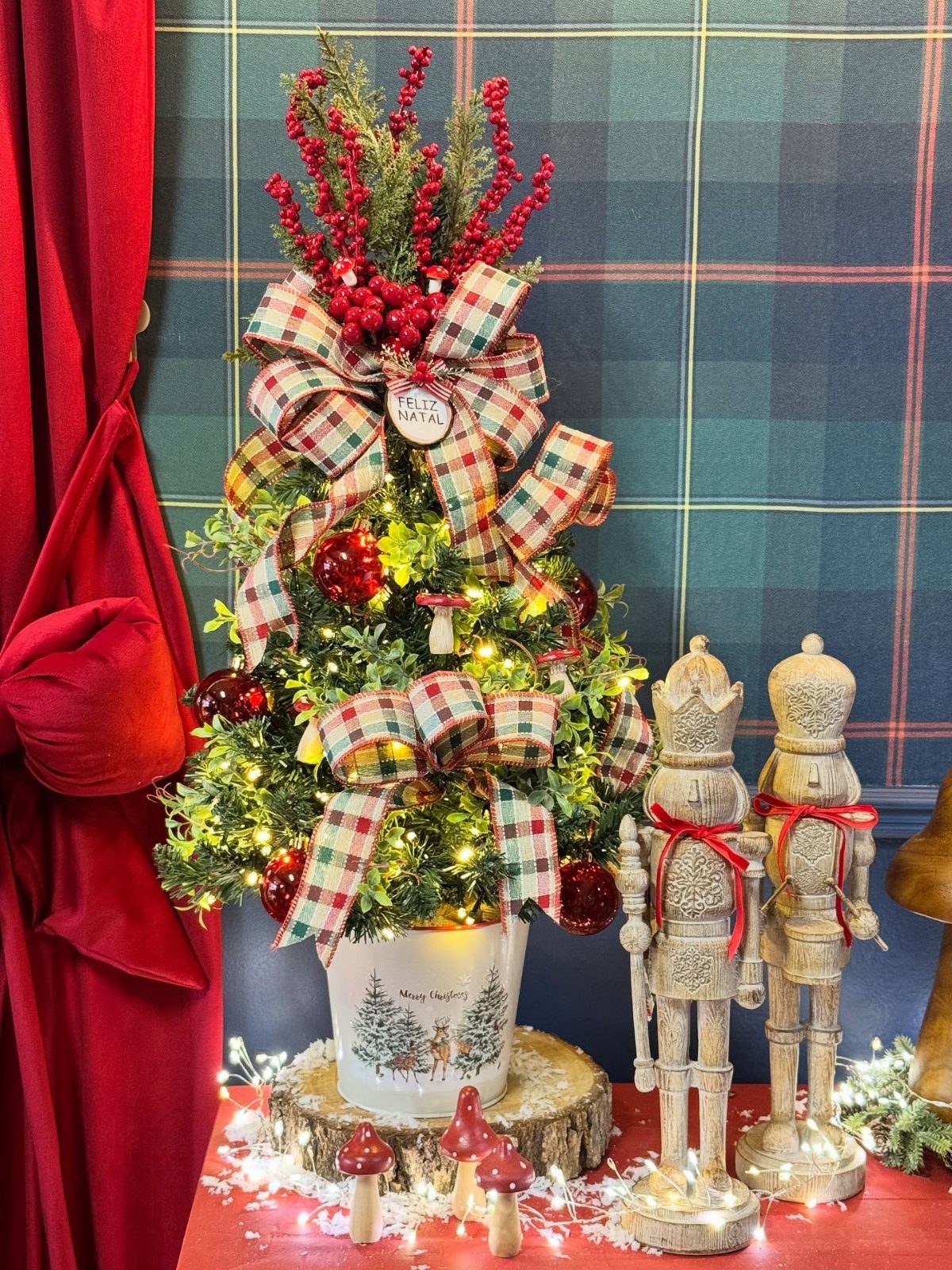 Small decorated Christmas tree with plaid bows and wooden nutcrackers on red surface