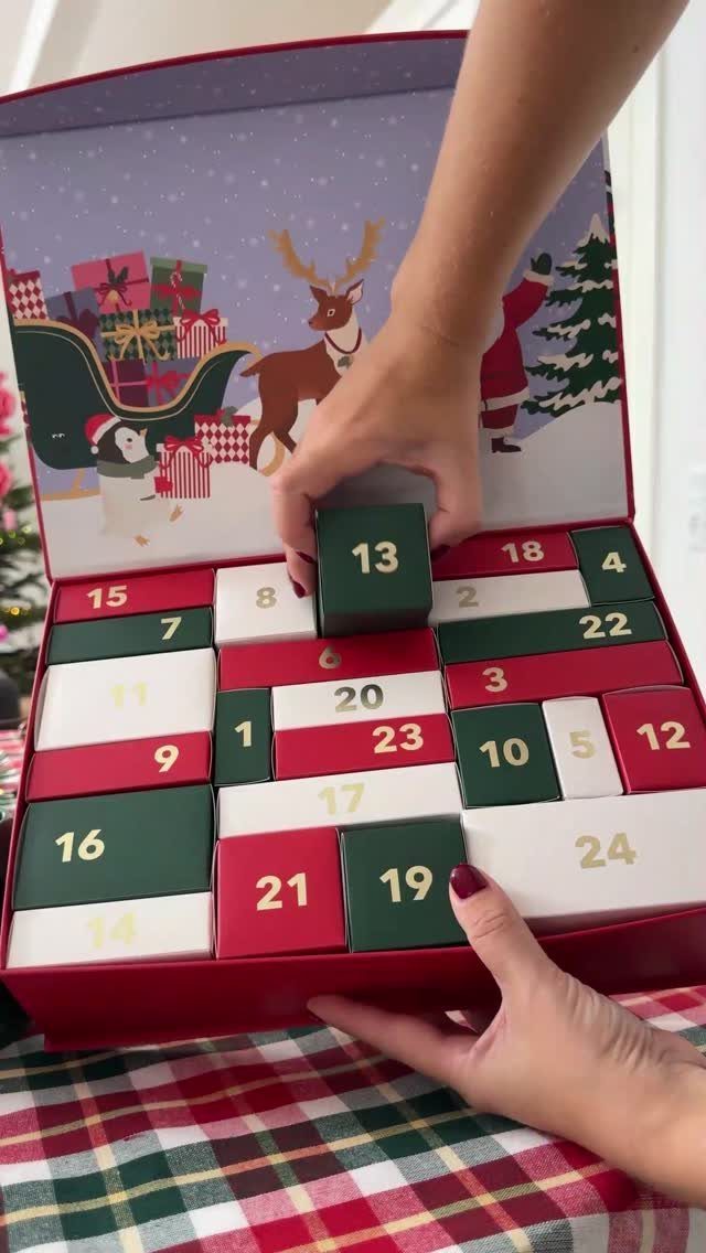 Hands arranging numbered red, green, and white blocks in a Christmas advent calendar box.