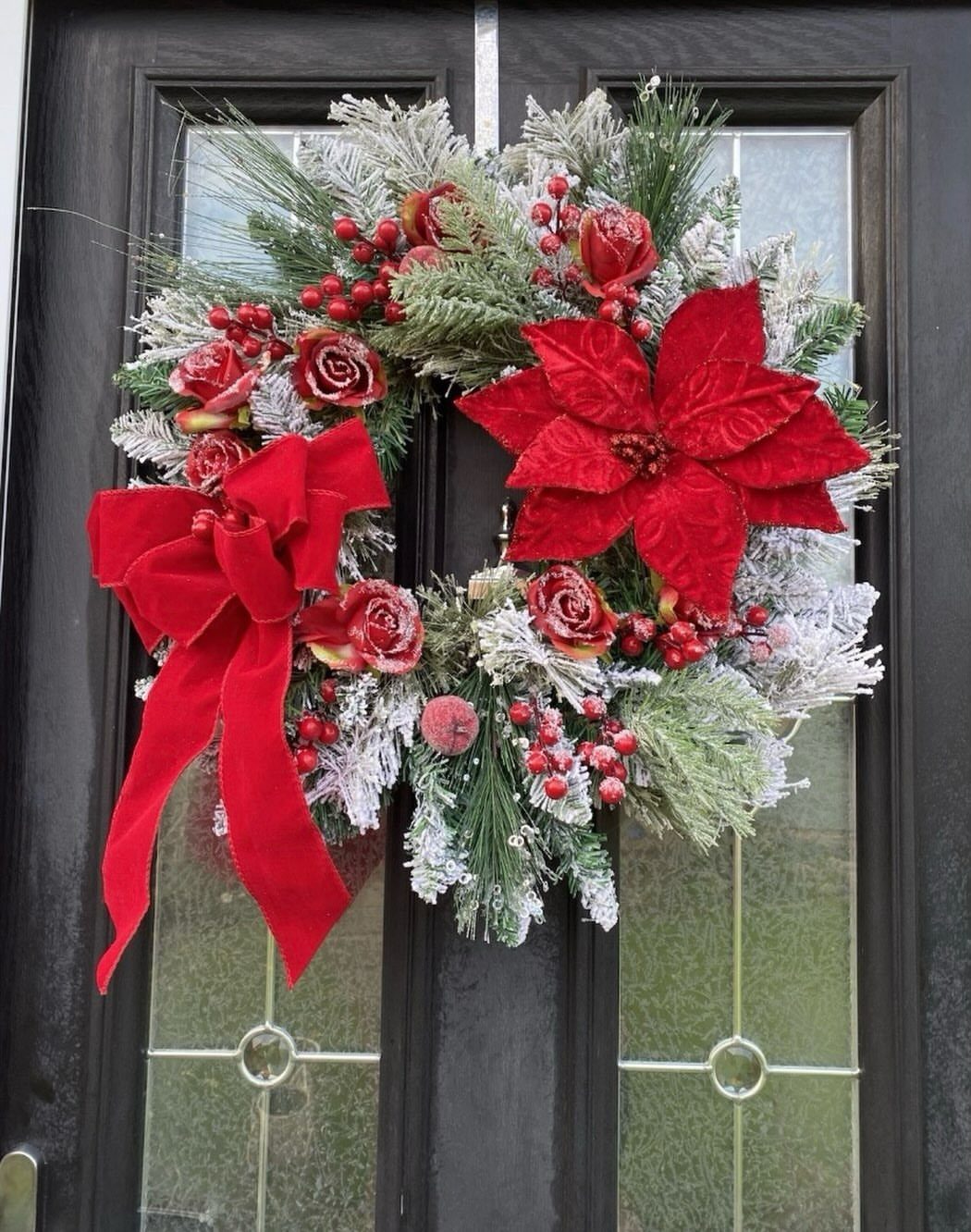 Frosted Christmas wreath with red poinsettias and a red bow on a black door