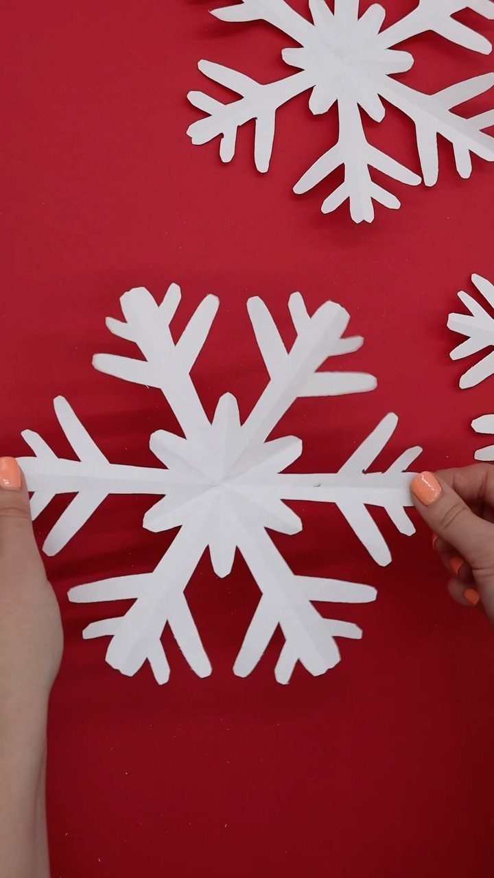 White paper snowflakes held by hands against a bright red background.