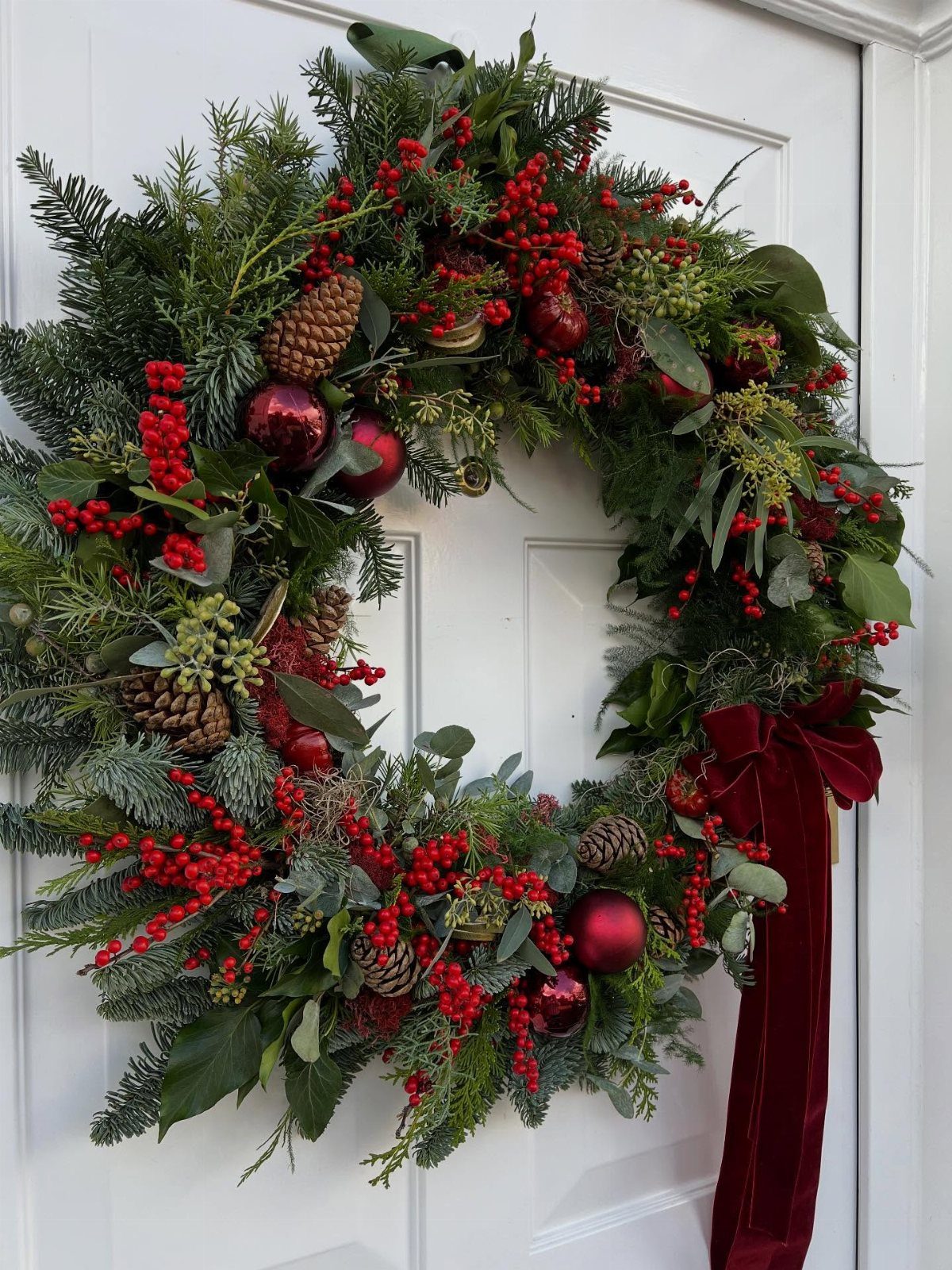 Green Christmas wreath with red berries and ornaments on a white door