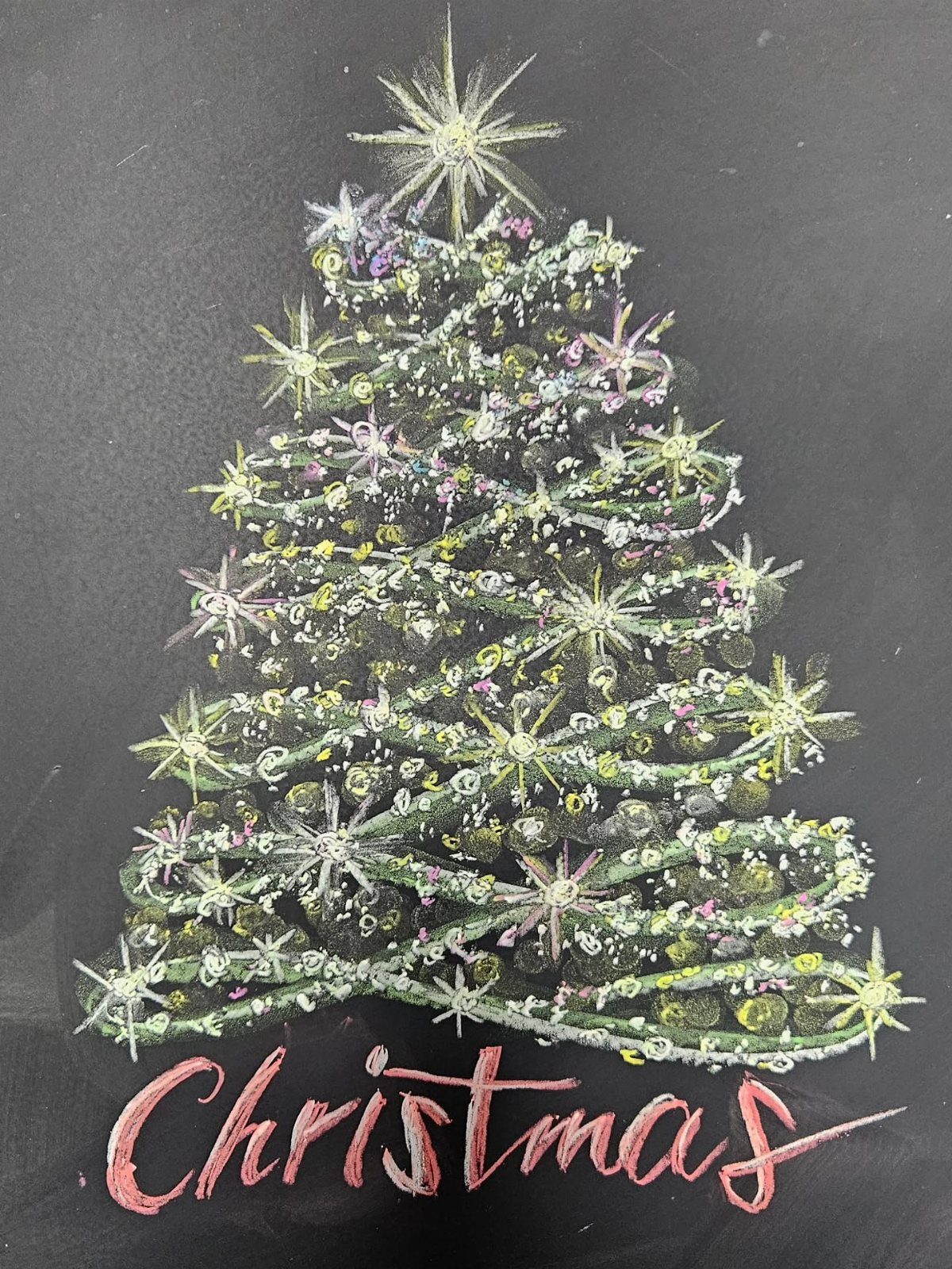 Chalk drawing of a decorated Christmas tree with red cursive text on chalkboard