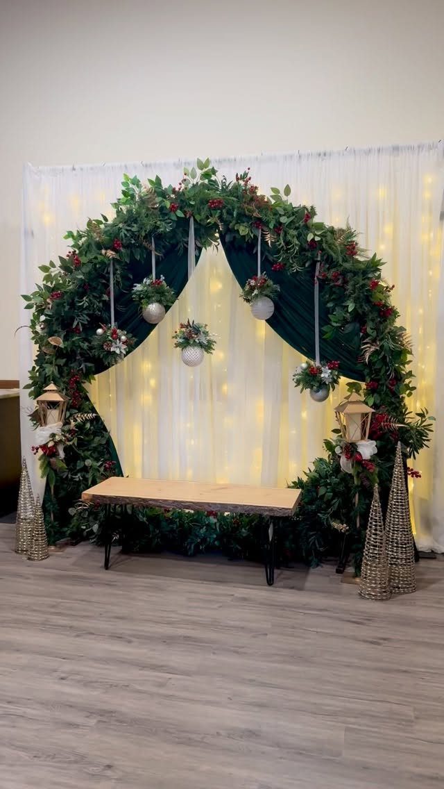 Circular greenery arch with fairy lights and a wooden bench for holiday photos.
